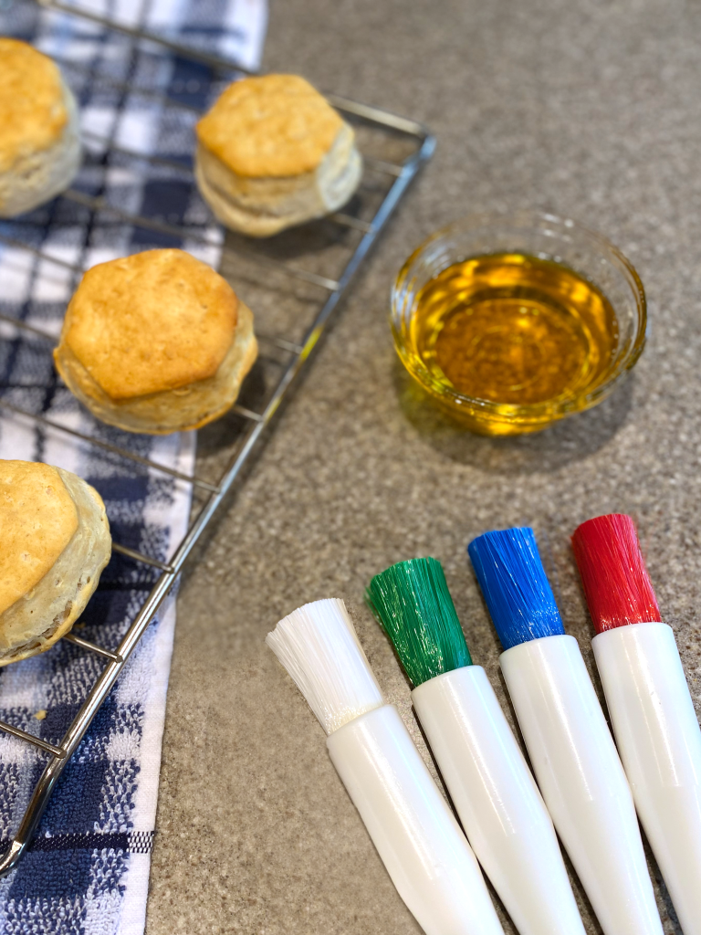 Four Pastry Brushes with bowl of melted butter and wire rack with biscuits